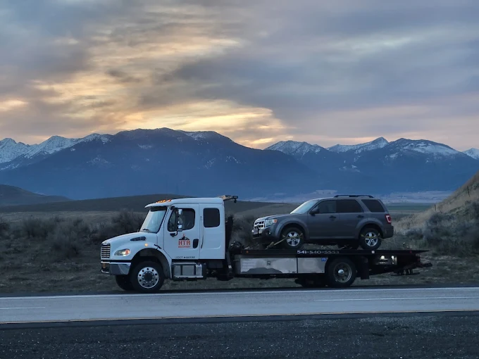 An HTR Recovery flatbed on the highway at dusk with a loaded SUV, snow-capped mountains behind it.
